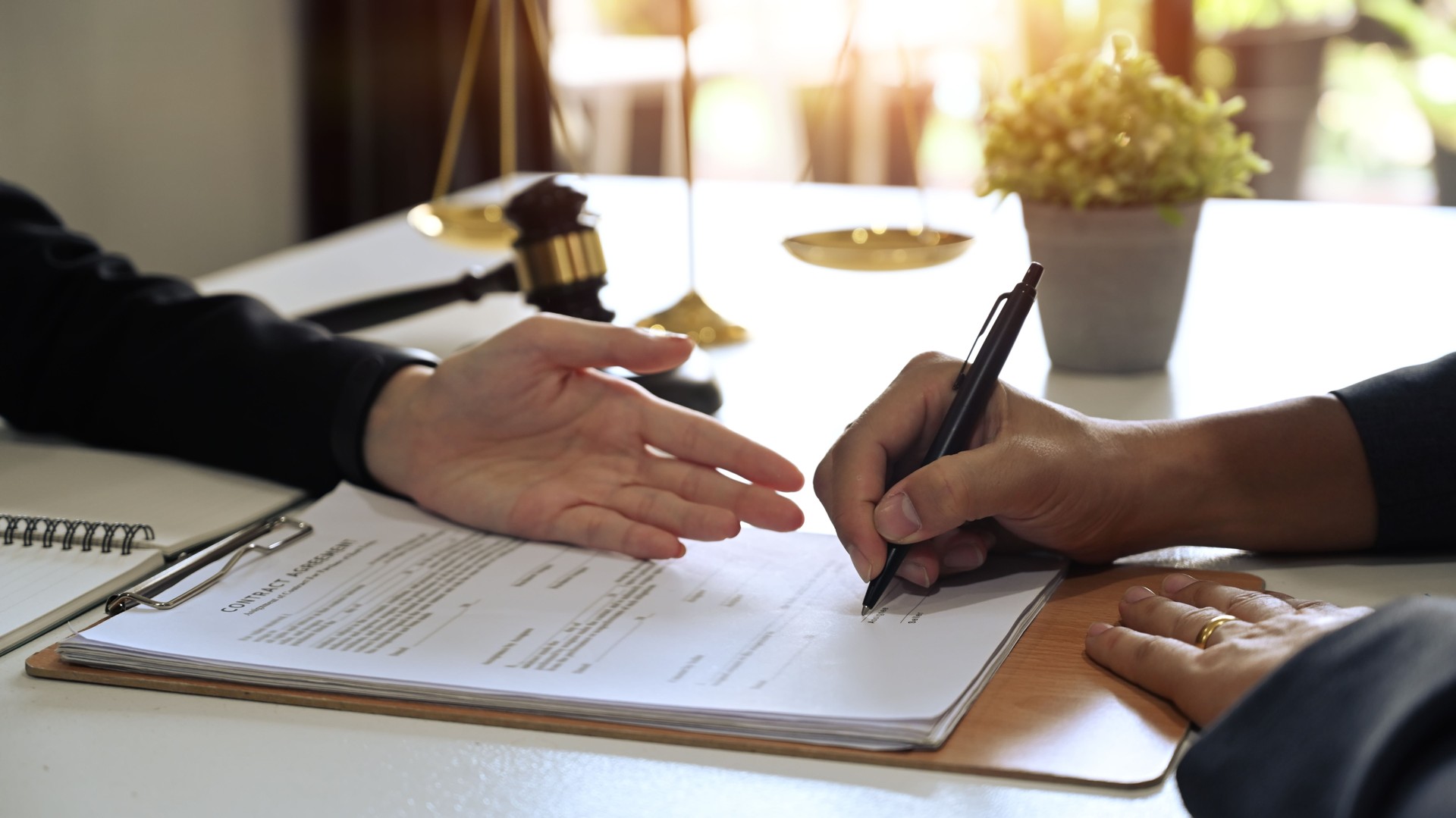 Young businessman signing agreement with skilled lawyer and showing place for signature on contract document.