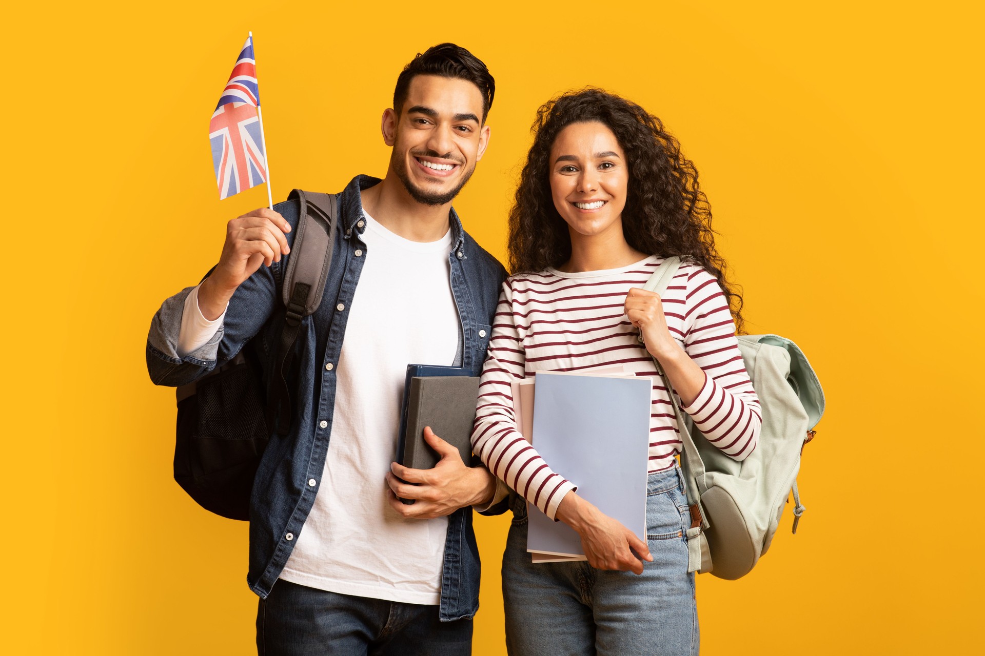Study Abroad. Young Arab Man And Woman With Backpacks Holding British Flag
