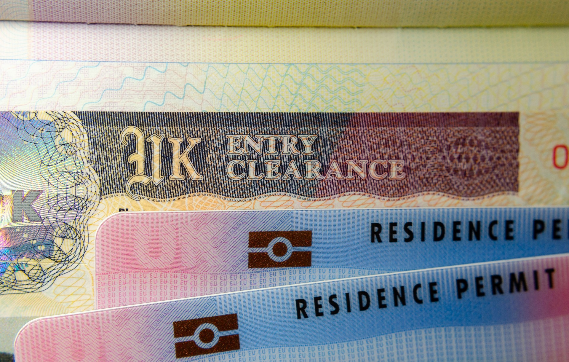 UK BRP (Biometrical Residence Permit) cards for Tier 2 work visa placed on top of UK Entry Clearance vignette sticker in the passport.